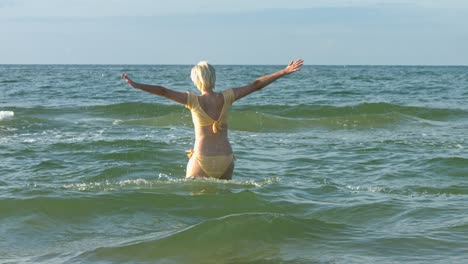 Eine-Frau-In-Einem-Pastellgelben-Bikini,-Die-Durch-Eine-Welle-Im-Meerwasser-Springt