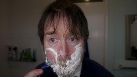 Close-up-of-caucasian-man-with-deep-blue-eyes-wet-shaving-his-face-with-beard-at-home-in-bathroom