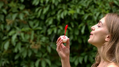 A-woman-blowing-bubbles-against-a-background-of-natural-green-hedge-plant
