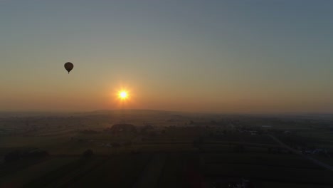 Sunrise-of-a-Hot-Air-Balloon-on-a-Misty-Morning-Over-Amish-Farmlands-as-Seen-by-a-Drone