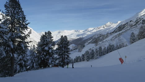 Pista-De-Esquí-Con-Esquiadores-Descansando-Y-Montañas-En-El-Fondo,-Panorámica