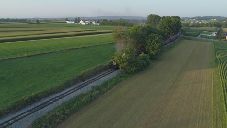 Aerial-View-of-a-1924-Steam-Engine-with-Passenger-Train-Traveling-Along-the-Amish-Countryside-as-the-Sunsets-on-a-Summer-Day-as-Seen-by-a-Drone