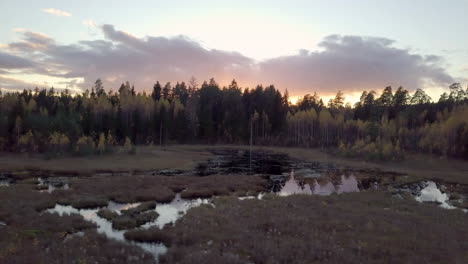 Low-aerial-shot-over-the-pond-towards-the-sunset-in-rural-area-of-Latvia,-Europe---Camera-movement-sideways-to-the-left