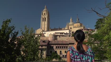 Slow-push-in-towards-back-of-female,-standing,-looking-at-Segovia-townscape-from-distance