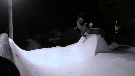 Snowboarder-Masculino-Haciendo-Trucos-En-Un-Parque-Construido-En-Su-Patio-Trasero-Por-La-Noche