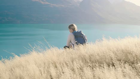Mädchen-Sitzt-Im-Goldenen-Gras-In-Den-Neuseeländischen-Bergen-Mit-Blick-Auf-Den-Blauen-See