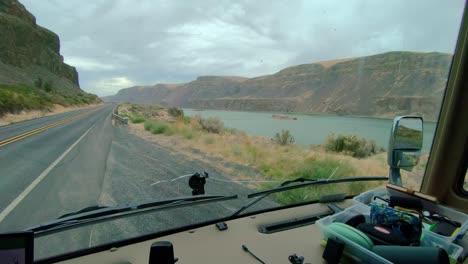 POV-of-the-driver-of-a-parked-Class-A-RV,-point-of-view-of-Lenore-Lake-and-Highway-17-in-Washington-State-on-a-cloudy,-windy-day