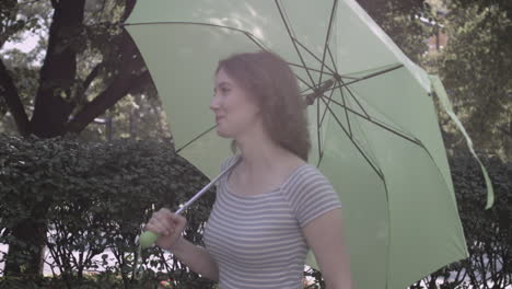 Millennial-Frau-Geht-An-Einer-Hecke-Entlang-Und-Trägt-Einen-Neongrünen-Regenschirm