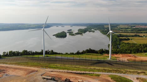 Aerial-static-shot-of-wind-turbines-moving-above-Susquehanna-River-on-summer-day,-renewable-energy-theme