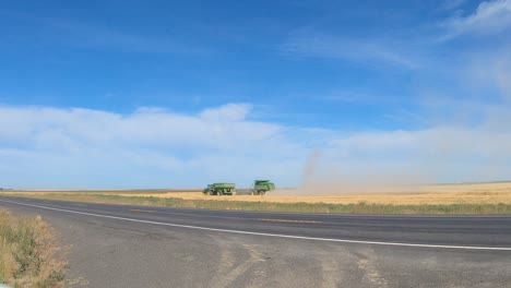 Combine-harvester-and-grain-wagon-are-harvesting-wheat-in-eastern-Washington-state-with-traffic-passing-in-the-foreground