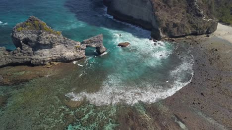 Luftaufnahme-Des-Atuh-Beach-Auf-Nusa-Penida,-Indonesien-An-Einem-Sonnigen-Tag-Und-Mit-Kristallblauem-Wasser,-Das-Auf-Die-Felsformationen-Trifft