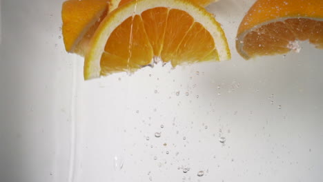 Refrescantes-Gajos-De-Naranja-Que-Caen-En-El-Agua,-Naranjas-Frescas-De-Color-Naranja-Vibrante