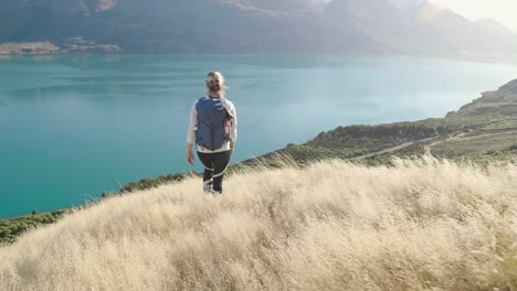 Niña-Caminando-En-Hierba-Dorada-En-Las-Montañas-De-Nueva-Zelanda-Con-Vistas-Al-Lago-Azul