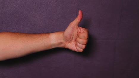 Male-hand-shows-fist-and-thumbs-up-on-black-background-behind-all-capture-in-120fps-slow-motion-movement-from-one-side-to-middle
