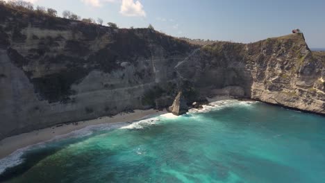 Luftaufnahme-Des-Kristallblauen-Wassers-Von-Diamond-Beach-In-Nusa-Penida,-Indonesien-Mit-Einer-Markanten-Großen-Klippe-Im-Vordergrund