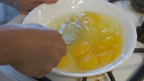 Woman-scrambles-eggs-in-white-bowl-with-whisk,-Slow-Motion