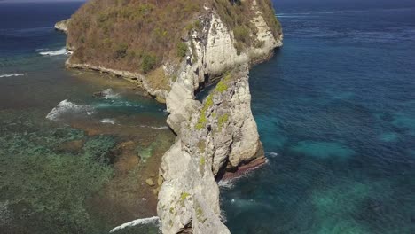 Aerial-view-of-Atuh-beach-on-Nusa-Penida,-Indonesia-on-a-sunny-day-and-with-crystal-blue-water-hitting-the-rock-formations