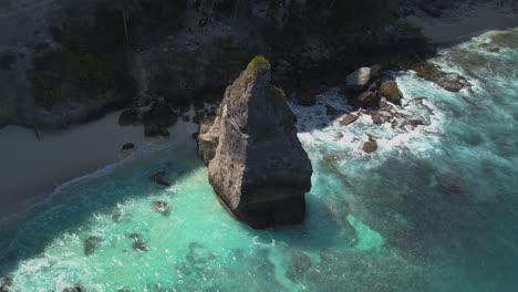 Aerial-view-of-the-crystal-blue-water-of-diamond-beach-in-Nusa-Penida,-Indonesia-with-a-prominent-large-cliff-in-the-foreground