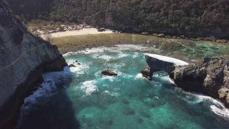 Aerial-view-of-Atuh-beach-on-Nusa-Penida,-Indonesia-on-a-sunny-day-and-with-crystal-blue-water-hitting-the-rock-formations