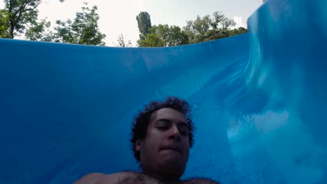 Face-and-chest-view-of-hairy-male-with-curly-hair-sliding-down-blue-waterslide
