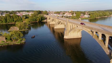 Reverse-aerial-drone-shot-of-traffic-traversing-bridge-above-Susquehanna-River,-fishermen-in-boat