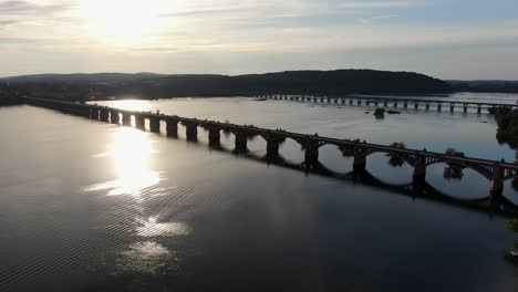 Aerial-push-in-shot-with-evening-sunset-reflecting-on-blue-waters-of-Susquehanna-River,-bridges-of-Route-462-and-Route-30