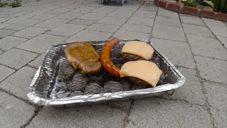 Locked-off-view-of-disposable-mini-BBQ-grill-with-different-and-cheesburger-on-tile-floor-SLOW-MOTION