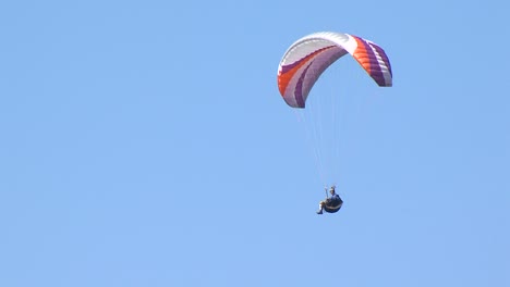 Paraglider-with-colorful-parachute-flies-across-blue-sky-on-summer-sunny-day