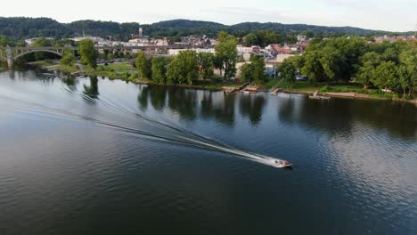 Drone-shot-following-a-racing-fishing-boat-on-Susquehanna-River-by-Columbia,-Pennsylvania-at-sunset,-wake-behind