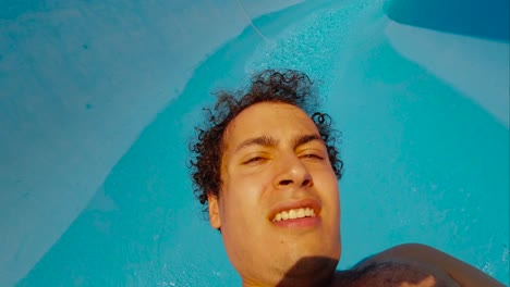 Face-and-chest-view-of-hairy-male-with-curly-hair-sliding-down-blue-waterslide-SLOW-MOTION