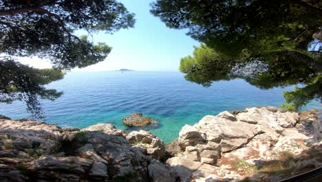 Beautiful,-hot,-sunny-day-view-over-sea-from-the-shaded-pine-treetops-with-rocky-coastline-beneath-your-feet