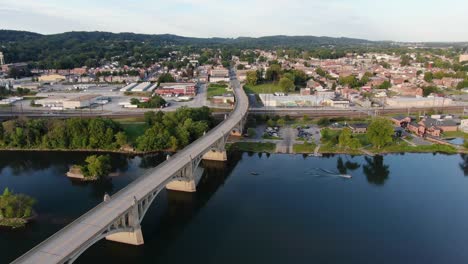 Aerial-turning-pan-of-Columbia,-Pennsylvania-with-smooth-blue-water-of-Susquehanna-River,-following-boat-leaving-wake,-clear-summer-evening