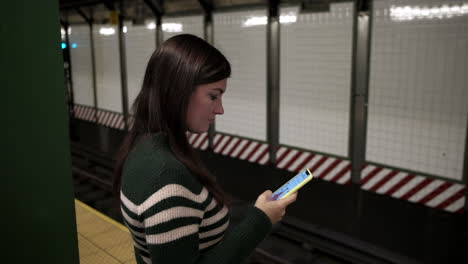 Young-Woman-uses-Social-media-on-smartphone-at-subway-station-while-waiting-for-the-subway-train-to-arrive