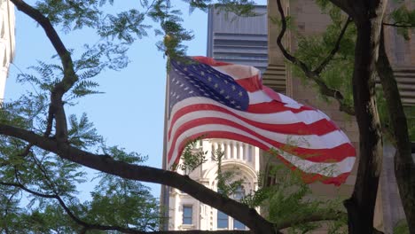 Slow-motion-shot-of-the-flag-of-the-USA-in-front-of-Trinity-Church-and-with-trees-in-the-foreground-at-summer-in-Manhattan,-New-York-City