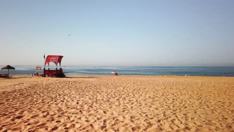 Villamoura-Strand-An-Der-Algarve-Portugal-Mit-Rettungsschwimmerstation-Und-Einsamem-Sonnenschirm-Kurz-Vor-Dem-Ende-Des-Tages