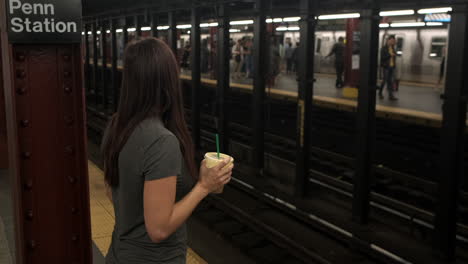 Young-Attractive-female-waits-for-subway-train-to-arrive-at-a-New-York-Subway-station-with-coffee-in-hand