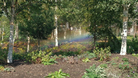 Sprinkler-system-in-wooded-area,-creating-a-rainbow-in-the-sunshine,-locked-off