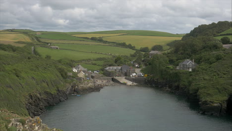 View-looking-down-of-historic-coastal-village-surrounded-by-lush-green-countryside,-Panning-shot
