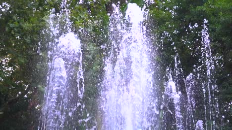 close-up-slow-motion-water-fountain-against-green-trees-and-nature,-shot-in-marbella,-malaga,-spain-at-120-fps
