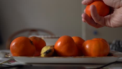 Juicy-satsumas-being-picked-up-off-of-a-plate-by-a-mans-hand,-close-up