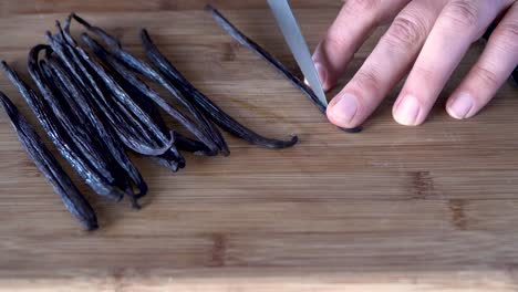 Slicing-vanilla-beans-with-a-knife-on-wooden-cutting-board,-close-up