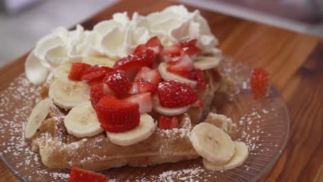 belgian-waffle-with-whipped-cream-strawberries-and-banana-being-eaten-by-a-young-woman-with-a-fork-and-knife,-tasty-dessert