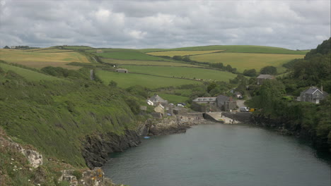 View-of-Port-Quin,-a-charming-coastal-village-with-rolling-fields-as-a-backdrop,-different-pov,-wide-panning-shot