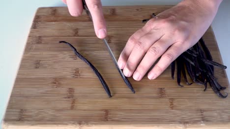 Above-view-hands-cutting-open-fresh-vanilla-bean-pods-with-knife