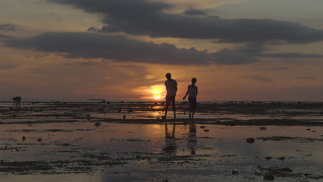 Silhouette-Von-Kindern,-Die-Fische-In-Einem-Sonnenuntergang-Am-Strand-Bei-Ebbe-Fangen-4k