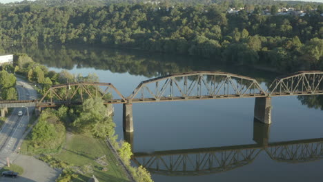 High-orbiting-drone-shot-of-a-rail-road-truss-bridge-crossing-a-river-at-sunrise