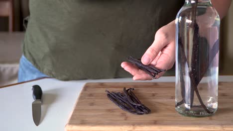 Woman-drops-vanilla-beans-into-glass-bottle-of-alcohol,-vanilla-extract