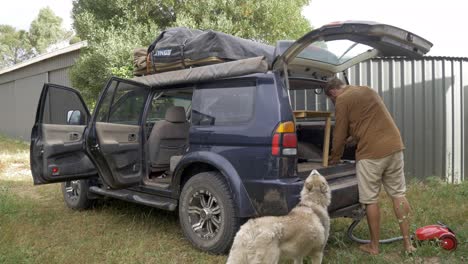 Man-with-dog-hoovering-inside-of-dirty-SUV-cleaning-vehicle-after-road-trip