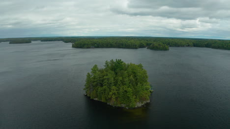 Drone-shot-of-small-island-in-the-middle-of-a-lake-with-a-cottage-on-it-on-a-dreary,-cool-day