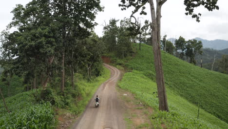 Man-driving-motorcycle-on-unpaved-dirt-road-in-green-countryside-mountains-of-Thailand